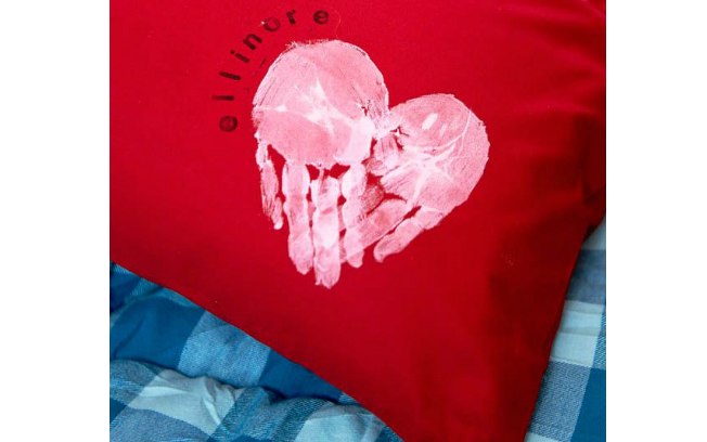As mãos da criança com tinta branca formam um coração na almofada vermelha