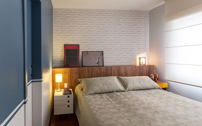 Um quarto aconchegante faz toda a diferença. A cabeceira em baú de madeira recebe papel de parede imitando tijolinho que conta com os quadros apoiados para finalizar a co