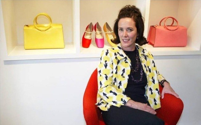 A estilista Kate Spade posando para foto atrás de algumas bolsas